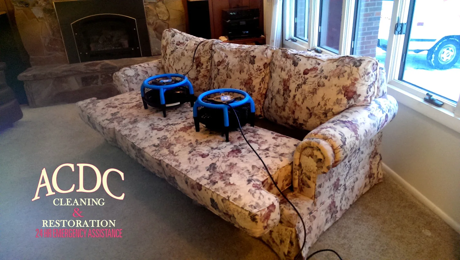 Freshly cleaned sofa drying under two air movers in a living room with a stone fireplace